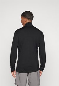 Camisa preta de manga longa com colarinho alto, feita de material suave, apresenta um design elegante e justo, com detalhes de costura mínimos.