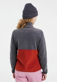 Fleece pullover met hoge kraag; grijze bovenkant en rode onderkant. Zachte textuur, lange mouwen en een getailleerd ontwerp.