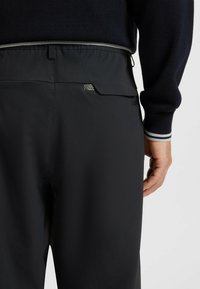Black trousers with a smooth, lightweight fabric. Features a slim fit, elastic waistband, and a small back pocket with logo detail.