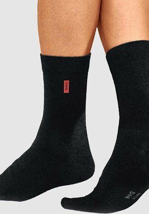 Schwarze Socken aus einem strukturierten Stoff, mit einem roten Logoetikett auf einer Seite. Knöchelhohes Design mit einem glatten, einheitlichen Erscheinungsbild.