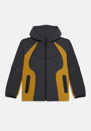 Mørk grå og sennepsgul hettejakke med frontglidelås og to glidelåslommer på sidene, designet for utendørs bruk.