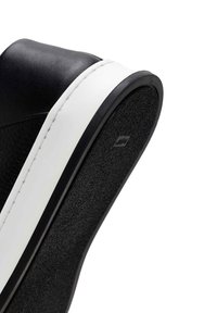 Black leather sneaker with a white rubber sole, featuring textured details and a smooth finish on the upper. Stitched white accents.