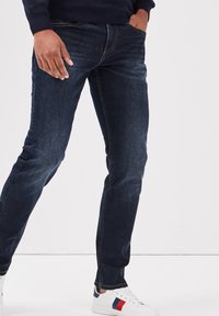 Donkerblauwe denim jeans met een slim fit, voorzien van een klassieke vijf-pocketontwerp en subtiele vervaging. Gecombineerd met witte sneakers.