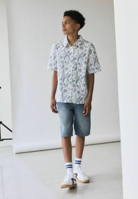 Camisa de manga corta con botones y un estampado botánico azul; combinada con pantalones cortos de mezclilla y zapatillas blancas con un acento negro y calcetas a rayas azules.