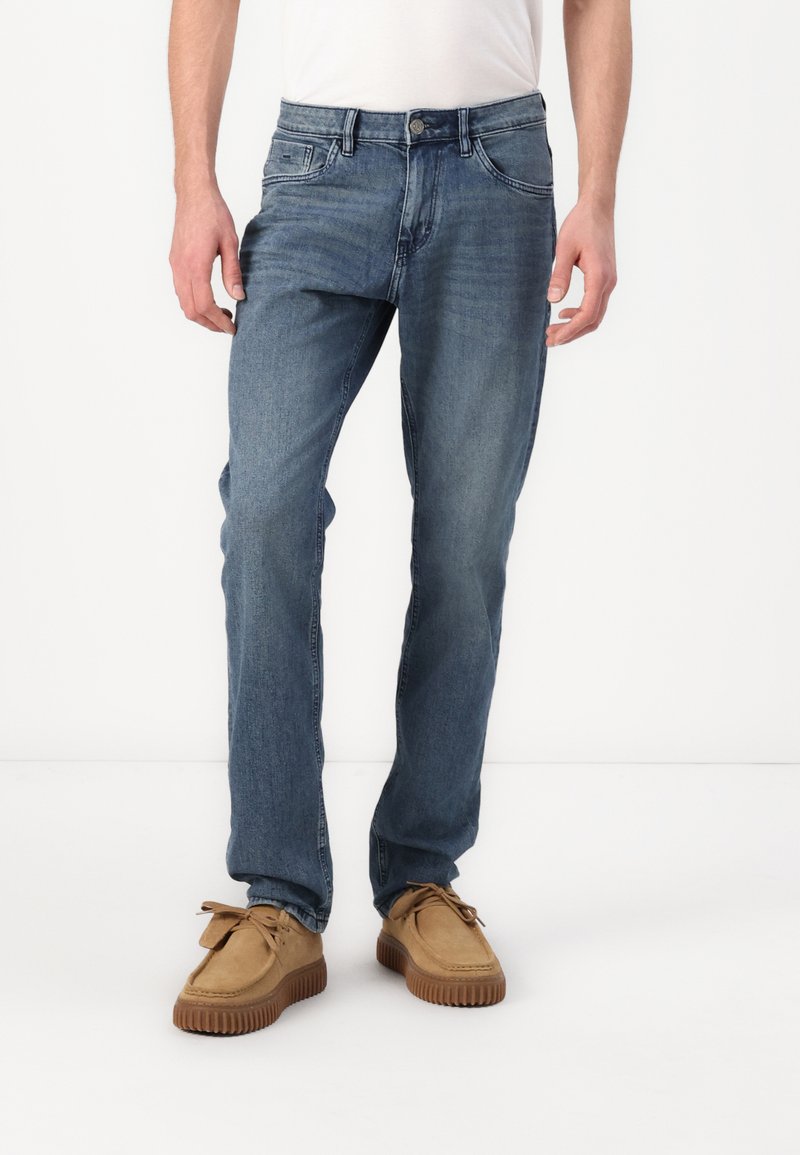 Jeans in denim blu con una vestibilità a gamba dritta, lavaggio chiaro, cinque tasche e cuciture color rame, abbinati a scarpe in stile mocassino color sabbia.