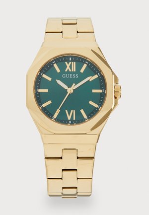 Montre-bracelet dorée avec un boîtier octagonal, un cadran vert, des marqueurs d'heure dorés et un bracelet en maillons métalliques. Nom de la marque affiché sur le cadran.