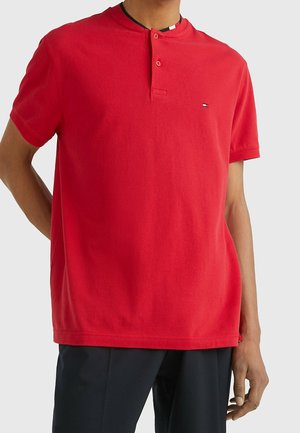 Polo a maniche corte rossa in cotone, con colletto henley e due bottoni, e un piccolo logo sul lato sinistro del petto.