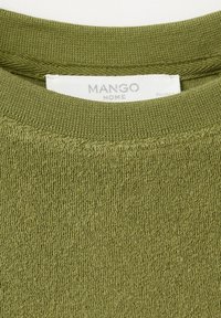 Green textured fabric close-up with MANGO HOME brand label stitched inside the collar of a knitted garment.