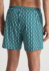 Zwemshorts in een turquoise en marineblauw geometrisch patroon, met een elastische tailleband en een lichtgewicht stof met een gladde textuur.