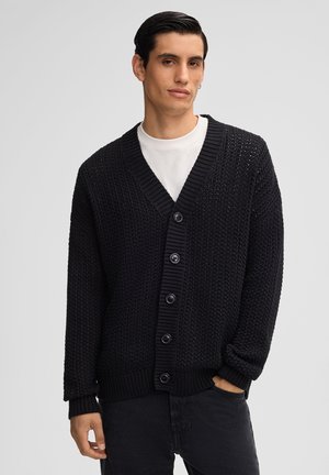 Cardigan nero lavorato a maglia con scollatura a V profonda, sei grandi bottoni e polsini e orlo a costine. Presenta un tessuto testurizzato con taglio comodo.