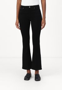 Melnas zābakveida bikses ar augstu jostasvietu, kas aprīkotas ar piecām kabatām, metāla pogu aizdari un mīkstu, nedaudz teksturētu audumu.