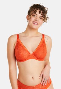 Bralette en dentelle orange avec un design en V, des bretelles ajustables et des détails de motif délicats. Coutures plates pour le confort et une finition lisse.
