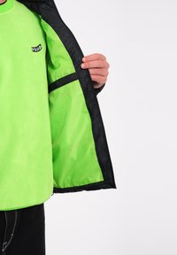 Felgroene fleece trui met zwarte accenten, voorzien van een rits en een binnenzak. Gladde textuur met een ronde halslijn.