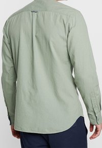 Langärmliges Hemd in Minzgrün mit Knopfkragen, Rückenpasse und abgerundetem Saum. Hergestellt aus weichem, strukturiertem Stoff.