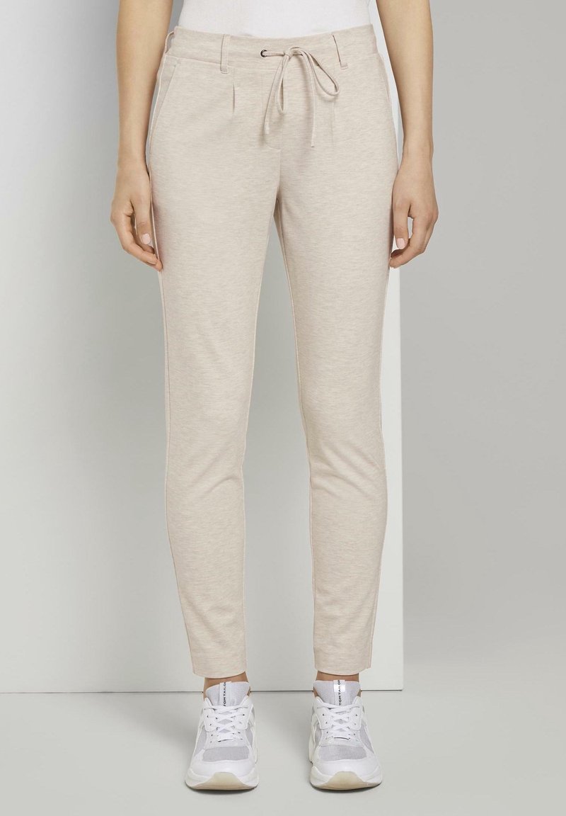 Ljust beigefärgade joggerbyxor tillverkade av mjukt, strukturerat tyg med elastisk midja och dragsko, med sidofickor och avsmalnande ben.