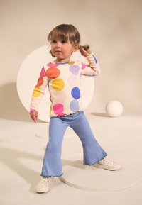 Dugotrajna majica s višebojnim točkicama, rebraste teksture; uparena sa svijetloplavim proširenim hlačama, zaokruženo bijelim tenisicama.