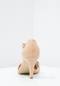 Kožené lodičky v nahé barvě s úzkým stilettem, uzavřenou patou a páskem kolem kotníku. Hladký povrch s lesklým povrchem.