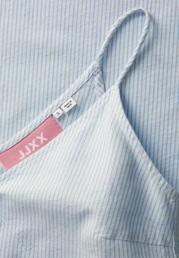 Camiseta sin mangas de rayas en azul claro con tirantes finos, que presenta una etiqueta rosa con la inscripción "JJXX", talla "S" y el texto "HECHO EN INDIA".
