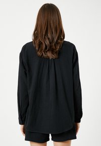 Mustapaitainen pitkähiha, jossa on teksturoitu materiaali, rento malli, takana pleat-yksityiskohta ja nappihihansuut, yhdistettynä matching shortsien kanssa.