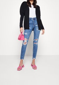 Černý pletený kardigan, bílý tričko, roztrhané modré skinny džíny, růžová kabelka a růžové sandály na podpatku s skládacími detaily.