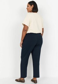 Krémový top s krátkým rukávem v kombinaci s tmavě modrými zúženými kalhotami, které mají hladkou texturu a minimalistický design. Oblečení doplňují baleríny se zvířecím vzorem.
