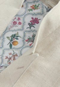 Beige kankaan tekstuuri, jossa on kukkakuosiset vuorikankaat, joissa on vaaleanpunaisia kukkia, vihreitä lehtiä ja keltaisia hedelmiä aallokkomaisessa suunnittelussa.