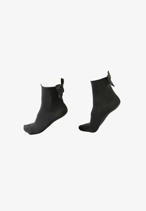Chaussettes noires à la cheville avec une finition texturée et un accent de nœud en satin au niveau de la cheville. Embout et talon renforcés pour plus de durabilité.