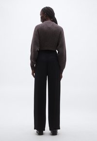 Un pulover maro tricotat cu mâneci bufante, asortat cu pantaloni evazați negri, cu talie înaltă, văzuți din spate.