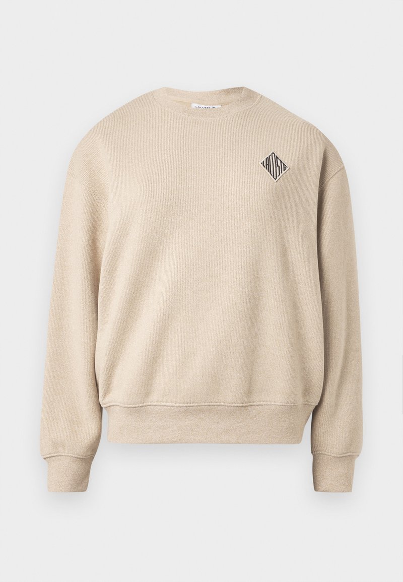 Beige sweatshirt met een geribbelde textuur, een ronde hals en een diamantvormig logo op de linkerborst. Lange mouwen met aansluitende manchetten.
