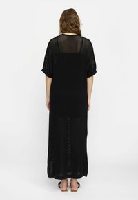 Schwarzes, langes, gestricktes Mesh-Kleid mit weiten Ärmeln und geradem Schnitt, das seitliche Schlitze für Bewegungsfreiheit bietet. Schlichtes und luftiges Design.
