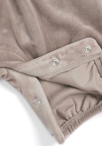 Gros plan d’un tissu doux beige avec des boutons-pression argentés et un bord élastique, probablement une partie d’un vêtement ou d’une couverture.