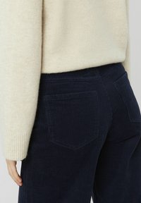 Pantalons en velours côtelé bleu marine avec des côtes verticales, dotés de poches arrière et d'une coupe ajustée, associés à un pull en tricot doux beige clair.