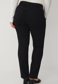 Schwarze Denim-Jeans mit einer taillierten Form, Fünf-Taschen-Design und genähten Details. Sie besitzen einen hohen Bund und eine leichte Stretch-Textur.
