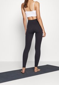 Czarne legginsy z wysokim stanem i biała krótka tank top, charakteryzujące się gładką teksturą i dopasowanym krojem, odpowiednie do odzieży sportowej.