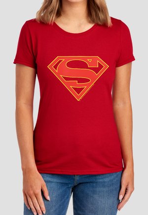 Woman wearing a red T-shirt with a large stylized red and yellow Superman logo on the chest, paired with blue jeans.