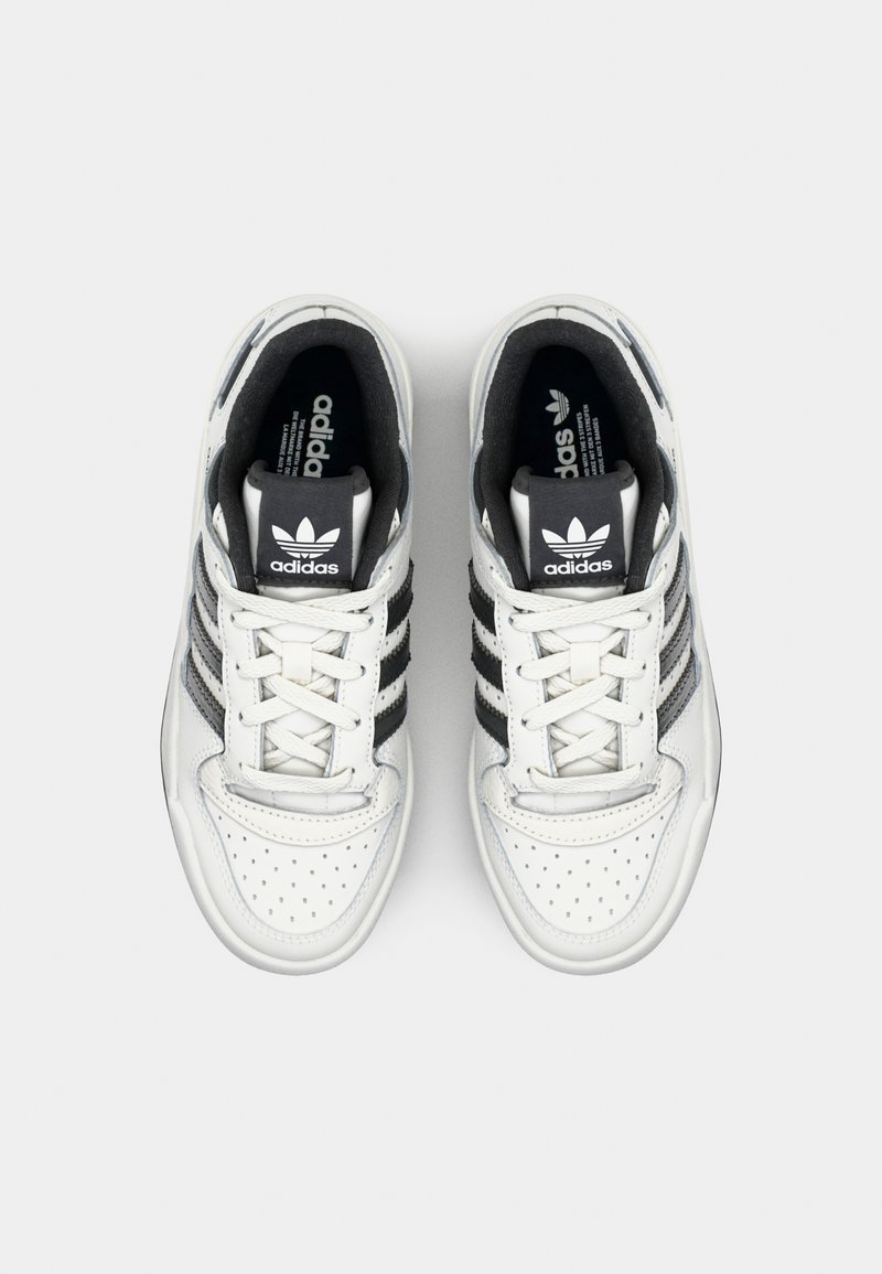 Witte leren sneakers met zwarte stoffen accenten, voorzien van drie verticale strepen, geperforeerde teepanelen en witte veters.