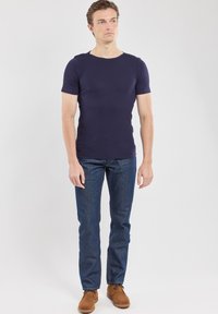 Maglietta a maniche corte blu navy in un design aderente, abbinata a jeans di denim blu e scarpe in camoscio marrone. Tessuto e taglio semplici e morbidi.