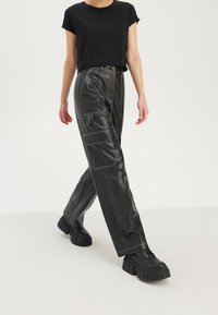T-shirt noir court associé à un pantalon noir en simili cuir taille haute avec des coutures blanches et des poches latérales. Des baskets noires épaisses complètent le look.