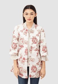 Chaqueta bordada floral en blanco con patrones de rosas rojas, que presenta un escote redondo, cinta de lazo y mangas acampanadas de tres cuartos.