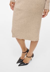 Beige räfflad midi klänning med långa ärmar, tillsammans med svarta lackläder klackar med spetsig tå och ankelsnören med gulddetaljer.