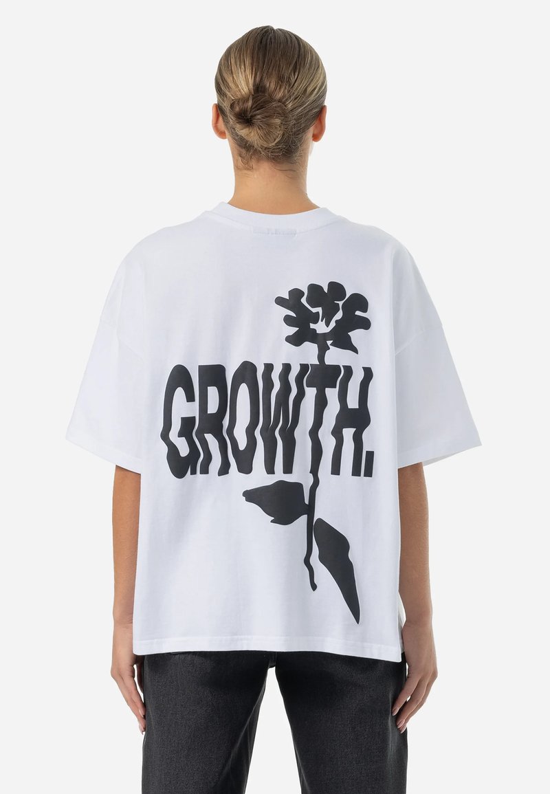 T-shirt blanc surdimensionné avec le texte graphique noir "GROWTH." et un design floral au dos. Manches courtes et coupe décontractée.