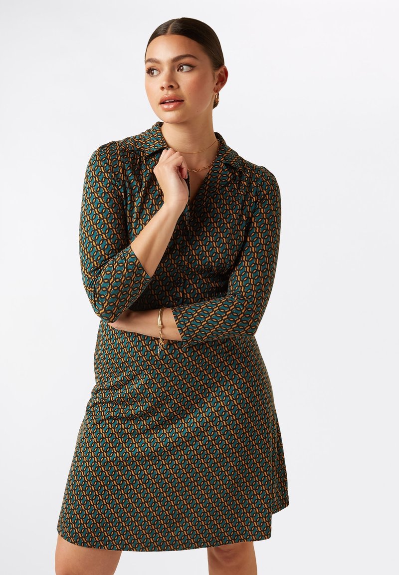 Vestido verde con estampado y mangas 3/4, que presenta un diseño geométrico en naranja y azul, hecho de una tela suave y ligera.