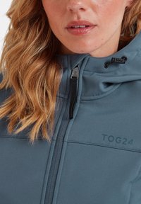 Blue zip-up jacket with a textured surface, featuring a hood, adjustable drawstring, and logo in a darker shade. No notable patterns evident.