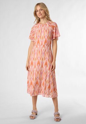 Maxikleid aus leichtem Stoff mit einem pink-orangefarbene abstrakten Muster, kurzen, flatternden Ärmeln und einem lockeren Schnitt. Kombiniert mit lila Blockabsatzsandalen.
