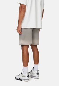 Shorts de sport gris avec une texture lisse, présentant un ourlet au-dessus du genou. Assortis à des baskets blanches et des chaussettes blanches arrivant aux chevilles.