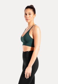 Mörkgrön sport-bh med djup V-ringning, justerbara band och sömlös design, kombinerad med högmidjade svarta leggings.