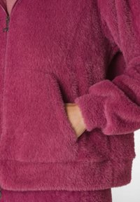 Giacca in pile con zip di colore rosa intenso, caratterizzata da una texture morbida e soffice, tasche frontali e polsini a costine sulle maniche e sull'orlo.