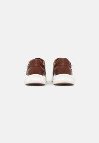 Brown leather sneakers with a textured white sole, featuring gold hardware detail at the heel. Smooth finish with subtle stitching accents.