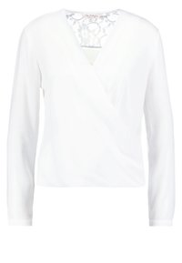 Blouse blanche à manches longues, portefeuille, col en V et détail en dentelle sur le haut du dos.