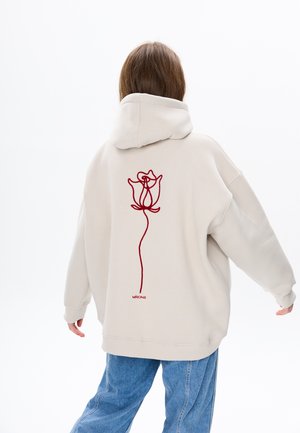 Beige hoodie met een rozenontwerp in donkerrood geborduurd op de rug. Heeft een relaxte pasvorm en een capuchon met trekkoord.
